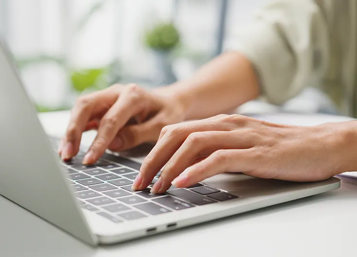 Close-up of a woman's hands typing on a laptop.